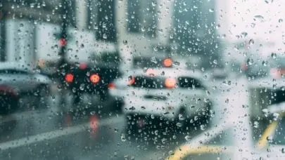 Rain droplets are the main focus as city traffic blurs by in the background, representing the article "Establishing Fault in a Rear-end Collision" by MMRBH Law Office.