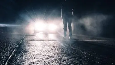 A person standing in the middle of the road as a car's headlights illuminate their form. This photo is meant to represent the article " Car Accidents and the Statute of Limitations in Louisiana" by MMRBH Law Office.