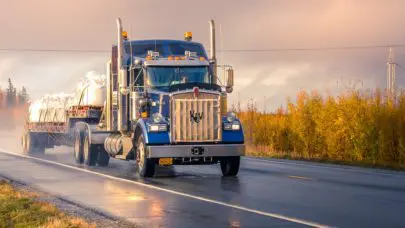 A large, flat-bed truck drives down a road wet from the rain, indicating one of the main causes of truck accidents.